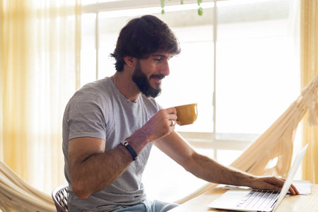Young business man working at home in his kitchen with laptop and papers on kitchen wooden desk. Gray notebook for working. Home office concept. high quality photoの写真素材