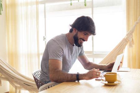 Young business man working at home in his kitchen with laptop and papers on kitchen wooden desk. Gray notebook for working. Home office concept. high quality photoの写真素材