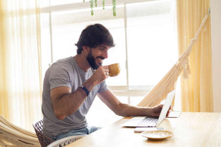 Young business man working at home in his kitchen with laptop and papers on kitchen wooden desk. Gray notebook for working. Home office concept. high quality photoの写真素材