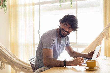Young business man working at home in his kitchen with laptop and papers on kitchen wooden desk. Gray notebook for working. Home office concept. high quality photoの写真素材