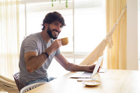Young business man working at home in his kitchen with laptop and papers on kitchen wooden desk. Gray notebook for working. Home office concept. high quality photoの写真素材