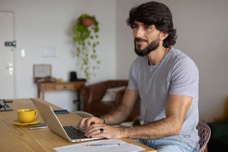 Young business man working at home in his kitchen with laptop and papers on kitchen wooden desk. Gray notebook for working. Home office concept. high quality photoの写真素材