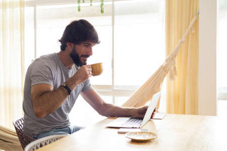 Young business man working at home in his kitchen with laptop and papers on kitchen wooden desk. Gray notebook for working. Home office concept. high quality photoの写真素材
