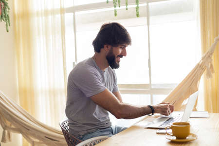Young business man working at home in his kitchen with laptop and papers on kitchen wooden desk. Gray notebook for working. Home office concept. high quality photoの写真素材