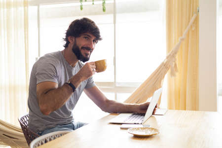 Young business man working at home in his kitchen with laptop and papers on kitchen wooden desk. Gray notebook for working. Home office concept. high quality photoの写真素材
