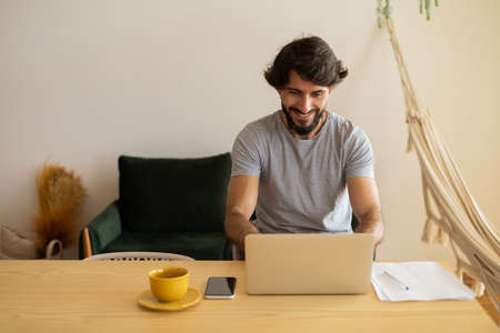 Young business man working at home in his kitchen with laptop and papers on kitchen wooden desk. Gray notebook for working. Home office concept. high quality photoの写真素材