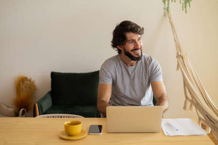 Young business man working at home in his kitchen with laptop and papers on kitchen wooden desk....