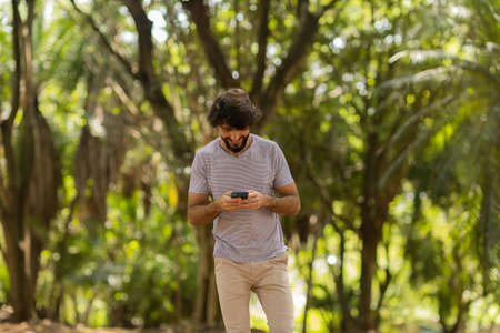 View of young man using a smartphone at day time with a green park in the background. Mobile phone, technology, urban concept. high quality photoの写真素材