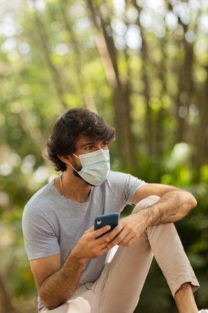 View of young man using a smartphone at day time with a green park in the background. Mobile phone, technology, urban concept. high quality photoの写真素材