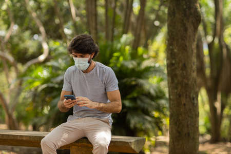 View of young man using a smartphone at day time with a green park in the background. Mobile phone, technology, urban concept. high quality photoの写真素材