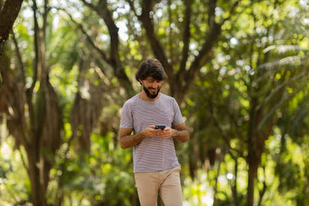 View of young man using a smartphone at day time with a green park in the background. Mobile phone, technology, urban concept. high quality photoの写真素材
