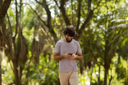 View of young man using a smartphone at day time with a green park in the background. Mobile phone, technology, urban concept. high quality photoの写真素材