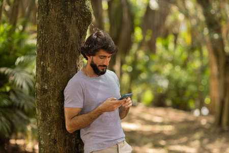 View of young man using a smartphone at day time with a green park in the background. Mobile phone, technology, urban concept. high quality photoの写真素材
