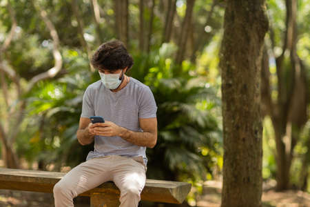 View of young man using a smartphone at day time with a green park in the background. Mobile phone, technology, urban concept. high quality photoの写真素材