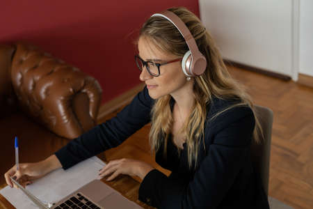 Young woman working at home with laptop and papers on desk and headphones. Home office concept. Gray notebook for working. high quality photoの写真素材
