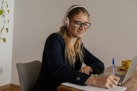 Young woman working at home with laptop and papers on desk and headphones. Home office concept. Gray notebook for working. high quality photoの写真素材