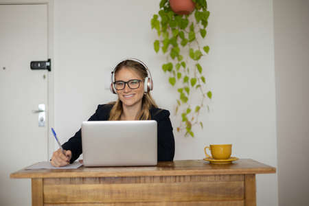 Young woman working at home with laptop and papers on desk and headphones. Home office concept. Gray notebook for working. high quality photoの写真素材