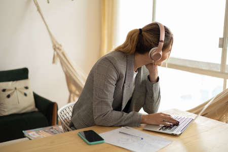 Young woman working at home with laptop and papers on desk and headphones. Home office concept. Gray...