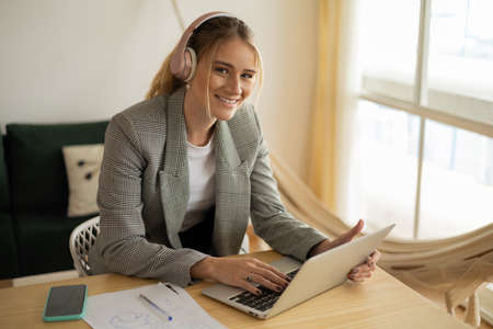 Young woman working at home with laptop and papers on desk and headphones. Home office concept. Gray notebook for working. high quality photoの写真素材