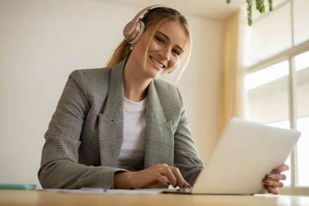 Young woman working at home with laptop and papers on desk and headphones. Home office concept. Gray notebook for working. high quality photoの写真素材