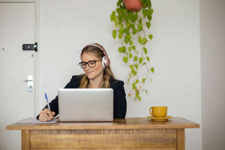 Young woman working at home with laptop and papers on desk and headphones. Home office concept. Gray notebook for working. high quality photoの写真素材