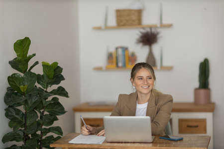Young woman working at home in her kitchen with laptop and papers on kitchen wooden desk. Home office concept. Gray notebook for working. Home office concept. high quality photoの写真素材