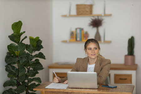 Young woman working at home in her kitchen with laptop and papers on kitchen wooden desk. Home office concept. Gray notebook for working. Home office concept. high quality photoの写真素材