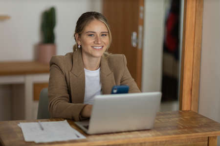 Young woman working at home in her kitchen with laptop and papers on kitchen wooden desk. Home office concept. Gray notebook for working. Home office concept. high quality photoの写真素材