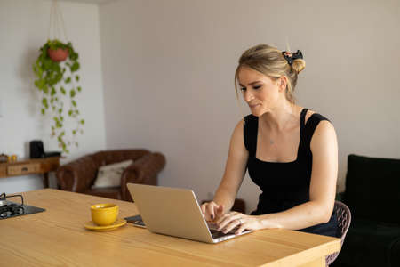 Young woman working at home in her kitchen with laptop and papers on kitchen wooden desk. Home office concept. Gray notebook for working. Home office concept. high quality photoの写真素材