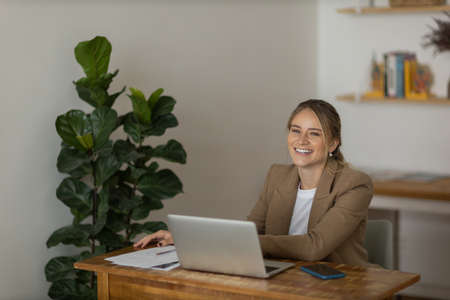 Young woman working at home in her kitchen with laptop and papers on kitchen wooden desk. Home office concept. Gray notebook for working. Home office concept. high quality photoの写真素材