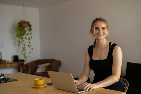 Young woman working at home in her kitchen with laptop and papers on kitchen wooden desk. Home office concept. Gray notebook for working. Home office concept. high quality photoの写真素材