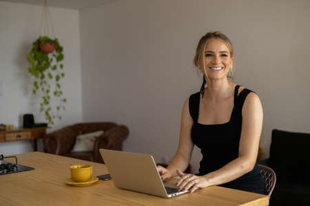 Young woman working at home in her kitchen with laptop and papers on kitchen wooden desk. Home office concept. Gray notebook for working. Home office concept. high quality photoの写真素材