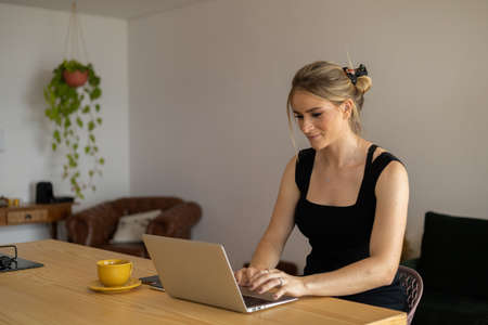 Young woman working at home in her kitchen with laptop and papers on kitchen wooden desk. Home office concept. Gray notebook for working. Home office concept. high quality photoの写真素材