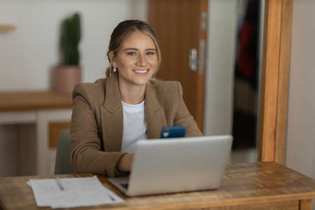 Young woman working at home in her kitchen with laptop and papers on kitchen wooden desk. Home office concept. Gray notebook for working. Home office concept. high quality photoの写真素材