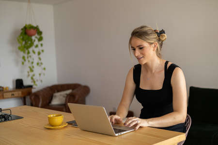 Young woman working at home in her kitchen with laptop and papers on kitchen wooden desk. Home office concept. Gray notebook for working. Home office concept. high quality photoの写真素材