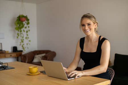 Young woman working at home in her kitchen with laptop and papers on kitchen wooden desk. Home office concept. Gray notebook for working. Home office concept. high quality photoの写真素材