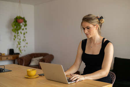 Young woman working at home in her kitchen with laptop and papers on kitchen wooden desk. Home office concept. Gray notebook for working. Home office concept. high quality photoの写真素材