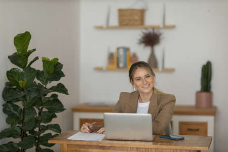 Young woman working at home in her kitchen with laptop and papers on kitchen wooden desk. Home office concept. Gray notebook for working. Home office concept. high quality photoの写真素材