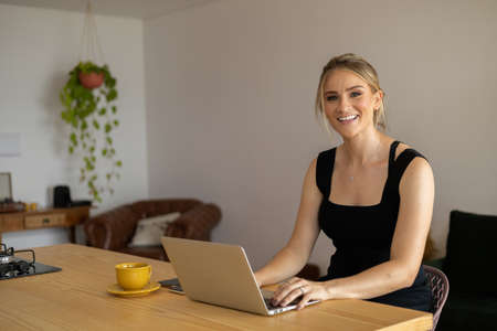 Young woman working at home in her kitchen with laptop and papers on kitchen wooden desk. Home office concept. Gray notebook for working. Home office concept. high quality photoの写真素材