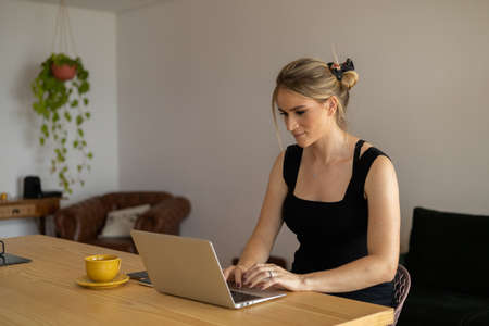 Young woman working at home in her kitchen with laptop and papers on kitchen wooden desk. Home office concept. Gray notebook for working. Home office concept. high quality photoの写真素材