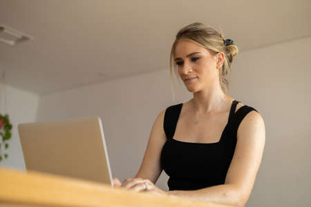 Young woman working at home in her kitchen with laptop and papers on kitchen wooden desk. Home office concept. Gray notebook for working. Home office concept. high quality photoの写真素材