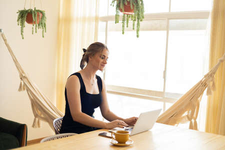 Young woman working at home in her kitchen with laptop and papers on kitchen wooden desk. Home office concept. Gray notebook for working. Home office concept. high quality photoの写真素材