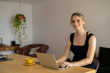 Young woman working at home in her kitchen with laptop and papers on kitchen wooden desk. Home office concept. Gray notebook for working. Home office concept. high quality photoの写真素材