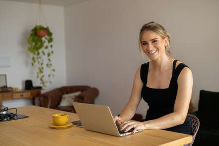 Young woman working at home in her kitchen with laptop and papers on kitchen wooden desk. Home office concept. Gray notebook for working. Home office concept. high quality photoの写真素材