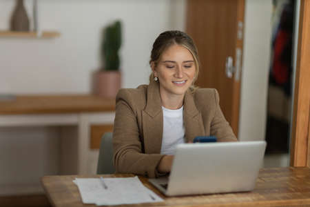 Young woman working at home in her kitchen with laptop and papers on kitchen wooden desk. Home office concept. Gray notebook for working. Home office concept. high quality photoの写真素材