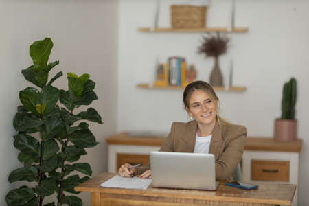 Young woman working at home in her kitchen with laptop and papers on kitchen wooden desk. Home office concept. Gray notebook for working. Home office concept. high quality photoの写真素材