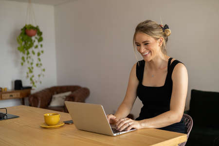 Young woman working at home in her kitchen with laptop and papers on kitchen wooden desk. Home office concept. Gray notebook for working. Home office concept. high quality photoの写真素材