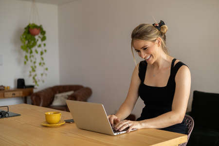 Young woman working at home in her kitchen with laptop and papers on kitchen wooden desk. Home office concept. Gray notebook for working. Home office concept. high quality photoの写真素材