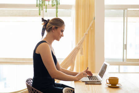 Young woman working at home from her living room couch with laptop on her lap. Home office concept. Gray notebook for working. Home office concept. high quality photoの写真素材