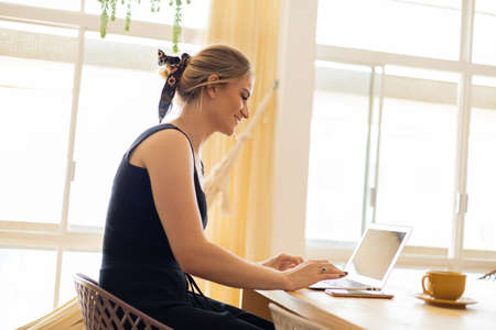 Young woman working at home from her living room couch with laptop on her lap. Home office concept. Gray notebook for working. Home office concept. high quality photoの写真素材